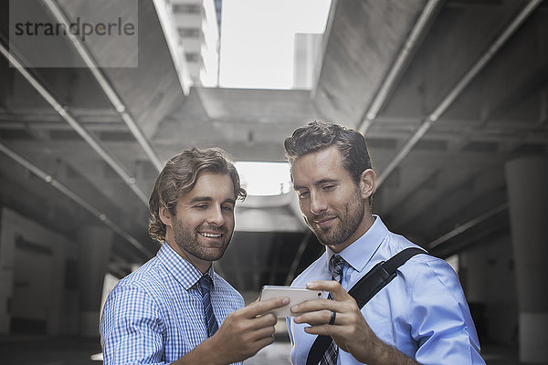 Zwei Männer in Hemd und Krawatte  die einen Selfie mit einem Smartphone nehmen  mit einem städtischen Gehweg und hohen Gebäuden im Hintergrund.