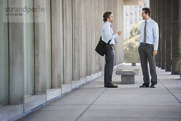 Zwei Geschäftsleute auf einem Gehweg vor einem Gebäude  im Gespräch.