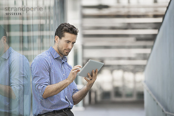 Ein Mann  der vor einem Gebäude mit großen Glasaußenwänden steht und ein digitales Tablett benutzt.