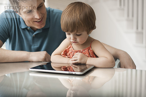 Ein Vater und seine Tochter schauen auf ein digitales Tablett  das über den Touchscreen bedient wird.