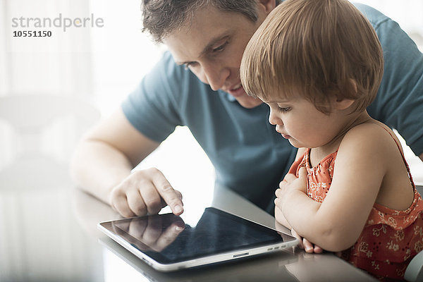 Ein Vater und seine Tochter schauen auf ein digitales Tablett  das über den Touchscreen bedient wird.