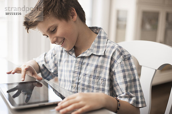 Ein Junge sitzt an einem Tisch mit einem digitalen Tablett  Hand auf dem Touchscreen.