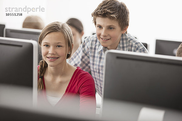 Ein Computer-Laborraum der Schule  mit Reihen von Bildschirmen. Zwei junge Leute schauen aufmerksam auf den Bildschirm.