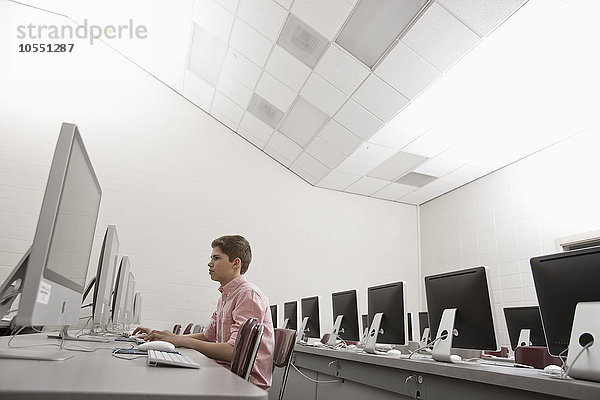 Ein Schulraum  ein Computerraum mit Bildschirmreihen und Sitzgelegenheiten. Eine junge Person  die an einem Terminal sitzt und arbeitet.