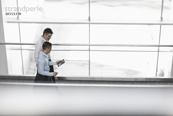 Zwei Männer stehen an den großen Fenstern eines Gebäudes und schauen auf den Bildschirm eines digitalen Tabletts.