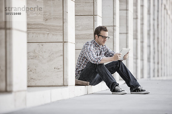 Ein Mann  der sich entspannt und sein Telefon überprüft  sitzt vor einem Gebäude.