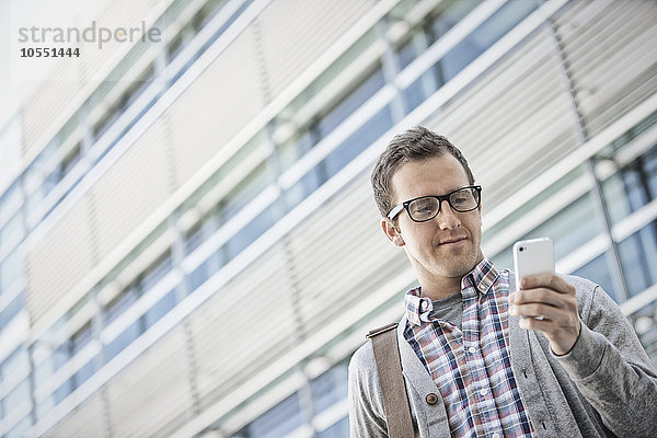 Ein Mann in einem karierten Hemd mit offenem Kragen  der sein Smartphone hält.