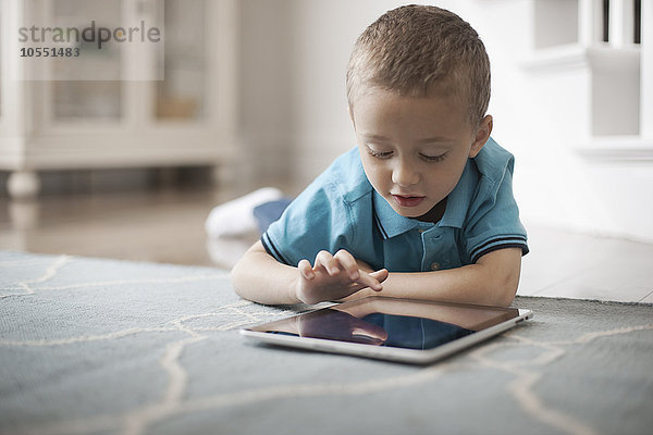 Ein Kleinkind  das an einem Tisch sitzt und ein digitales Tablett mit einem Touchscreen benutzt.