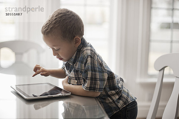 Ein Kleinkind  das an einem Tisch sitzt und ein digitales Tablett mit einem Touchscreen benutzt.