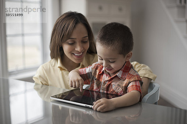 Eine Mutter und ihr Kind schauen auf den Bildschirm eines digitalen Tabletts  der Junge berührt den Bildschirm.