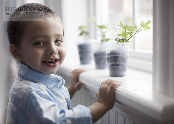 Ein kleiner Junge betrachtet junge Pflanzen in Töpfen  die auf einer Fensterbank wachsen.