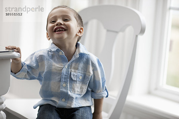 Ein kleiner Junge sitzt auf einem Stuhl  lächelt und schaut auf.