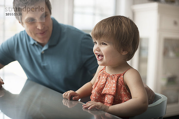 Ein Mann und ein kleines Kind sitzen an einem Tisch  Seite an Seite.