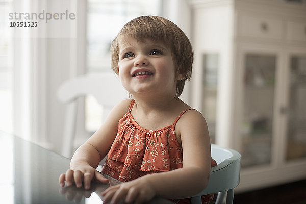 Ein kleines Kind  ein Mädchen  das an einem Tisch sitzt  aufschaut und lächelt.