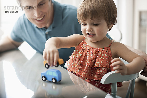 Ein Mann und ein kleines Kind sitzen und spielen mit Spielzeugautos.