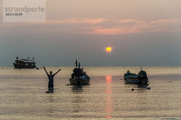 Junger Mann im Wasser mit zwei Longtail Booten  Südchinesisches Meer bei Sonnenuntergang  Golf von Thailand  Insel Koh Tao  Thailand  Asien