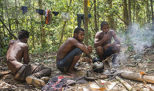 Drei junge Männer der Ureinwohner Orang Asil sitzen auf dem Boden im Dschungel und rauchen  indigenes Volk  tropischer Regenwald  Nationalpark Taman Negara  Malaysia  Asien