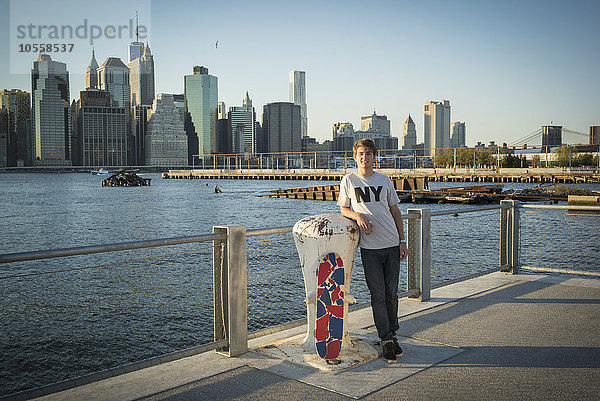 Kaukasischer Skateboarder lächelnd am Wasser  New York  Vereinigte Staaten