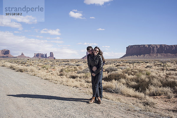 Kaukasisches Paar  das sich auf einer unbefestigten Straße in der Wüste umarmt