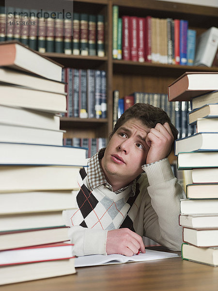 Student starrt auf Bücherstapel in der Bibliothek