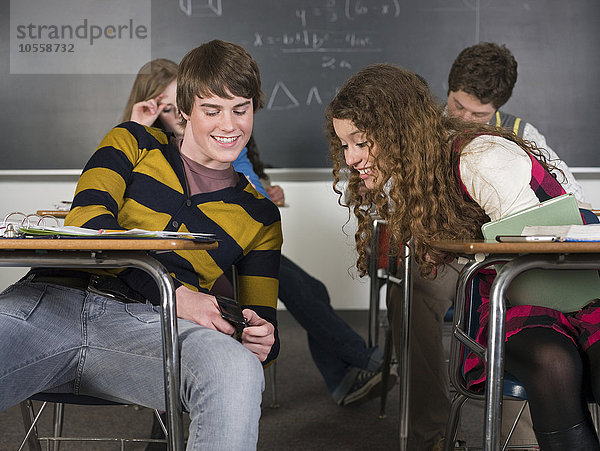 Schüler benutzen Mobiltelefon am Schreibtisch im Klassenzimmer