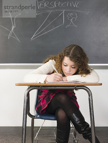 Schüler schreibt Notizen am Schreibtisch im Klassenzimmer