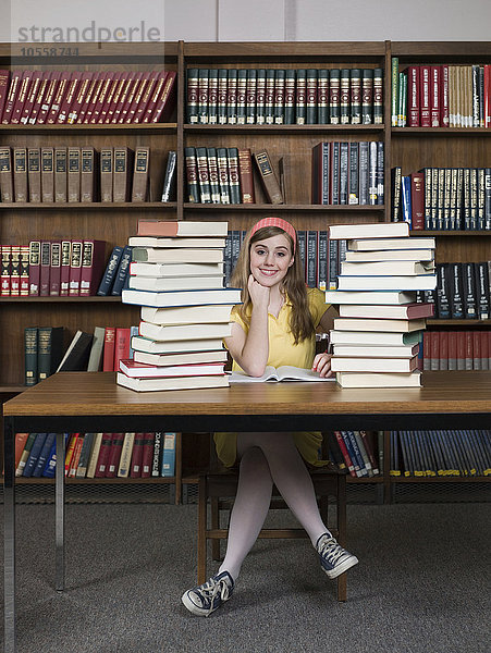 Studentin sitzt mit Büchern in der Bibliothek