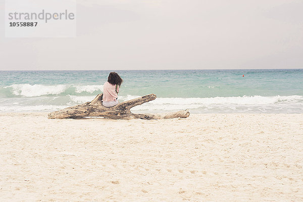 Frau sonnt sich auf einem Treibholzstamm am Strand