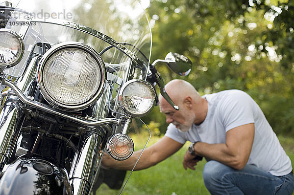 Älterer Mann repariert Motorrad im Park