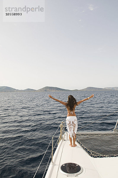 Frau steht mit ausgestreckten Armen auf dem Deck eines Segelbootes