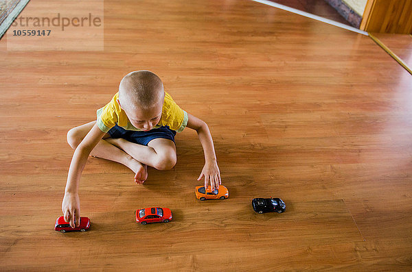 Kaukasischer Junge spielt mit Spielzeugautos auf dem Boden