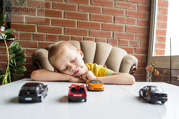 Kaukasischer Junge spielt mit Spielzeugautos am Schreibtisch