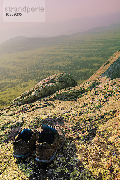 Nahaufnahme von Turnschuhen auf einer felsigen Hügelkuppe in einer abgelegenen Landschaft