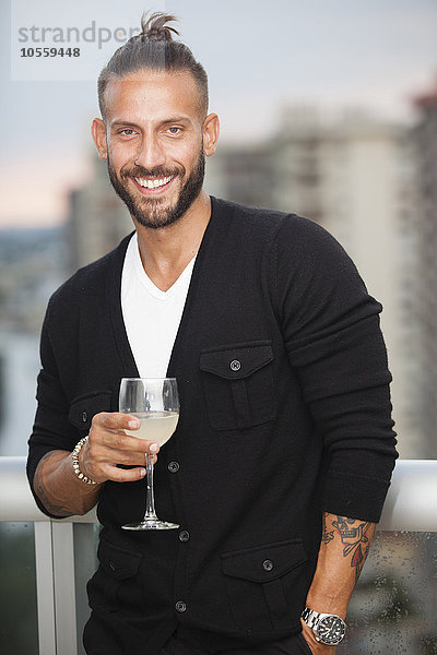 Hispanischer Mann trinkt Wein auf einem städtischen Balkon