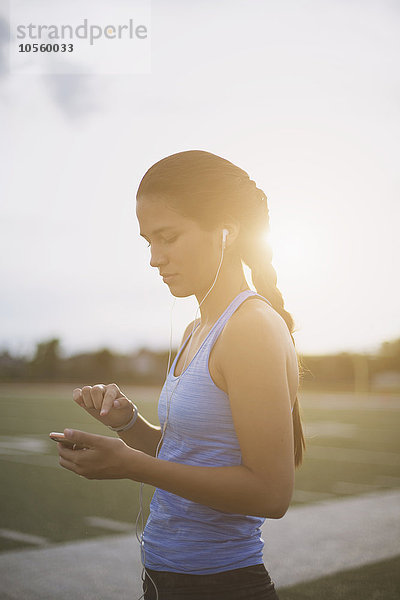 Gemischtrassiger Sportler hört auf dem Sportplatz einen mp3-Player