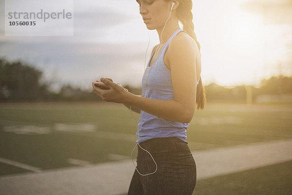 Gemischtrassiger Sportler hört auf dem Sportplatz einen mp3-Player