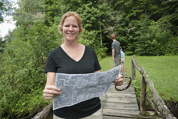 Kaukasische Frau liest auf einem Steg im Wald eine Karte