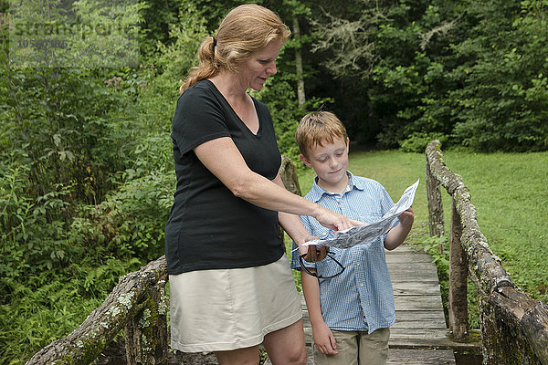 Kaukasische Mutter und Sohn lesen Karte auf einem Steg im Wald