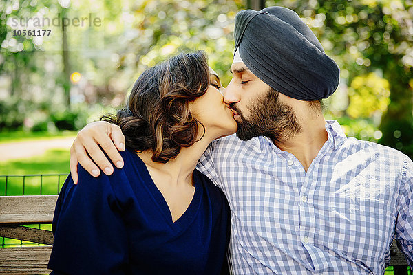 Indisches Paar küsst sich auf einer Bank im Stadtpark