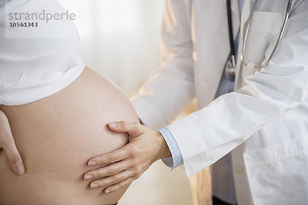 Arzt untersucht den Bauch einer schwangeren Frau