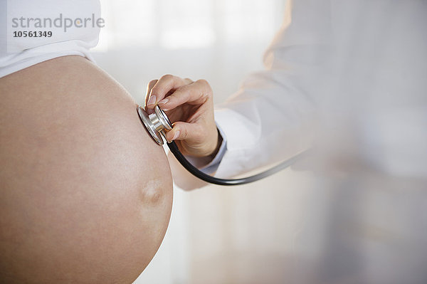 Arzt hört den Bauch einer schwangeren Frau mit einem Stethoskop ab