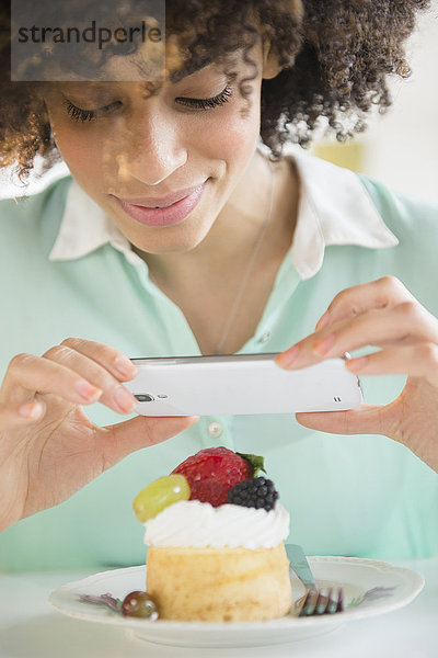 Gemischtrassige Frau  die ein Handyfoto vom Dessert macht