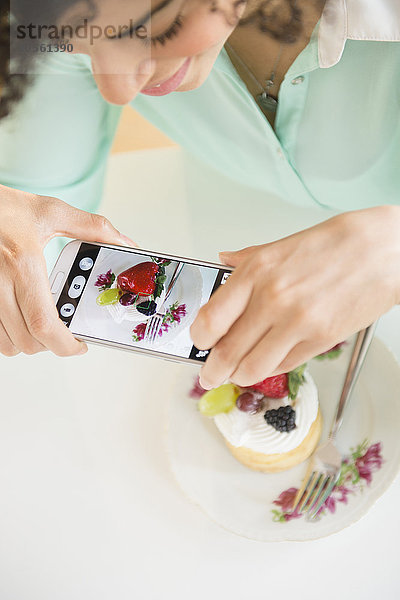 Gemischtrassige Frau  die ein Handyfoto vom Dessert macht