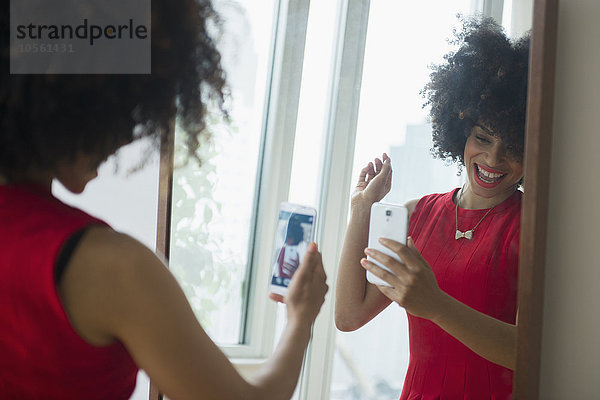 Gemischtrassige Frau macht Selfie mit Handy im Spiegel