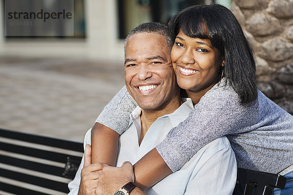 Afroamerikanischer Vater und Tochter umarmen sich auf einer Bank