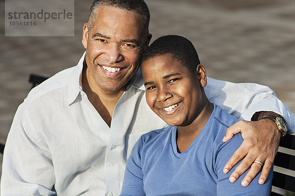 Afroamerikanischer Vater und Sohn umarmen sich auf einer Bank