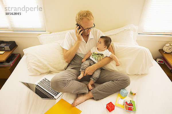 Vater hält seinen Sohn und spricht auf dem Bett mit dem Handy