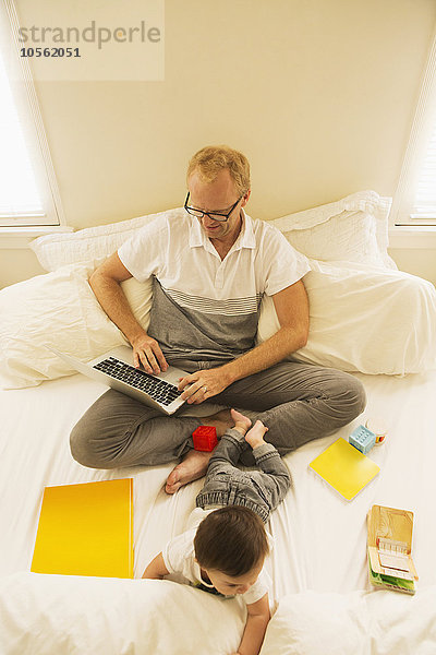 Vater benutzt Laptop und spielt mit Sohn auf dem Bett