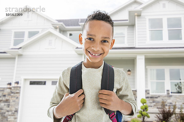 Schwarzer Junge mit Rucksack lächelt vor dem Haus