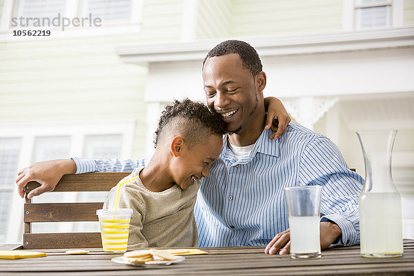 Schwarzer Vater und Sohn umarmen sich am Tisch im Hinterhof